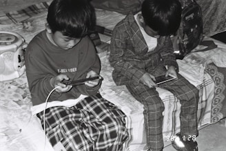 two young boys sitting on a bed looking at their cell phones