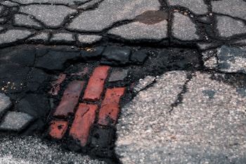 Cracked pavement exposes red bricks beneath, with surrounding asphalt showing signs of wear and decay.