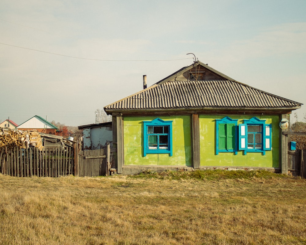 a small yellow house with blue windows in a field