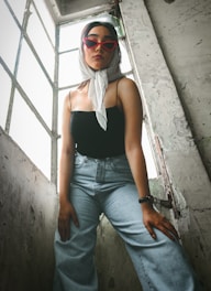 a woman wearing sunglasses and a scarf standing in front of a window