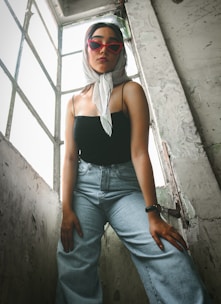 a woman wearing sunglasses and a scarf standing in front of a window