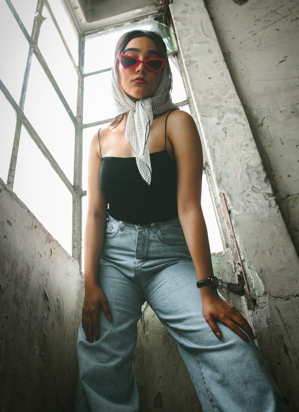 a woman wearing sunglasses and a scarf standing in front of a window