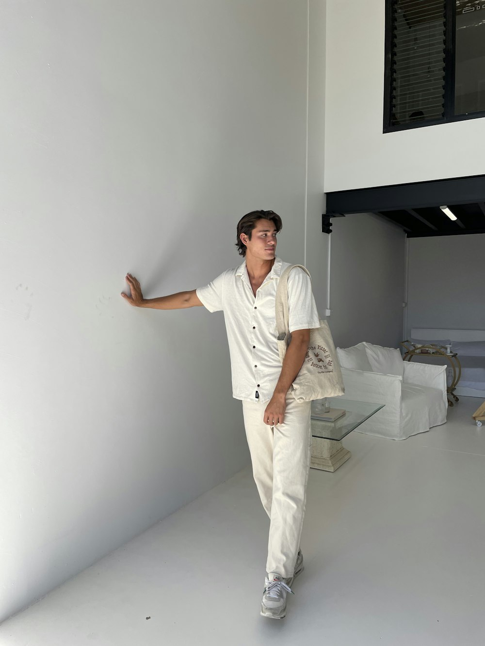 a man in a white shirt and pants leaning against a wall