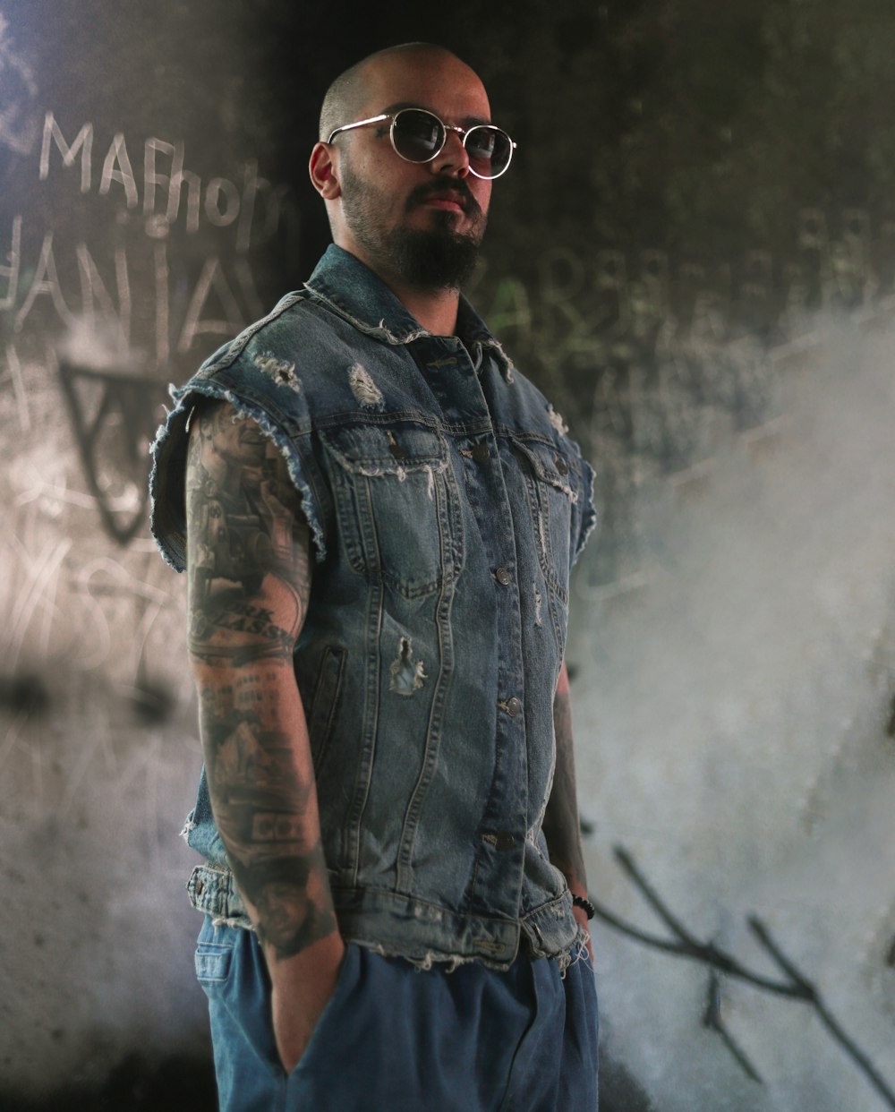 a man in a denim vest and sunglasses standing in front of a wall