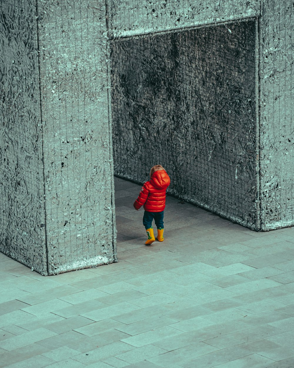 a small child in a red jacket and yellow boots