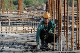 Smiling construction worker holding a CSCS green labourer card outside a building site.