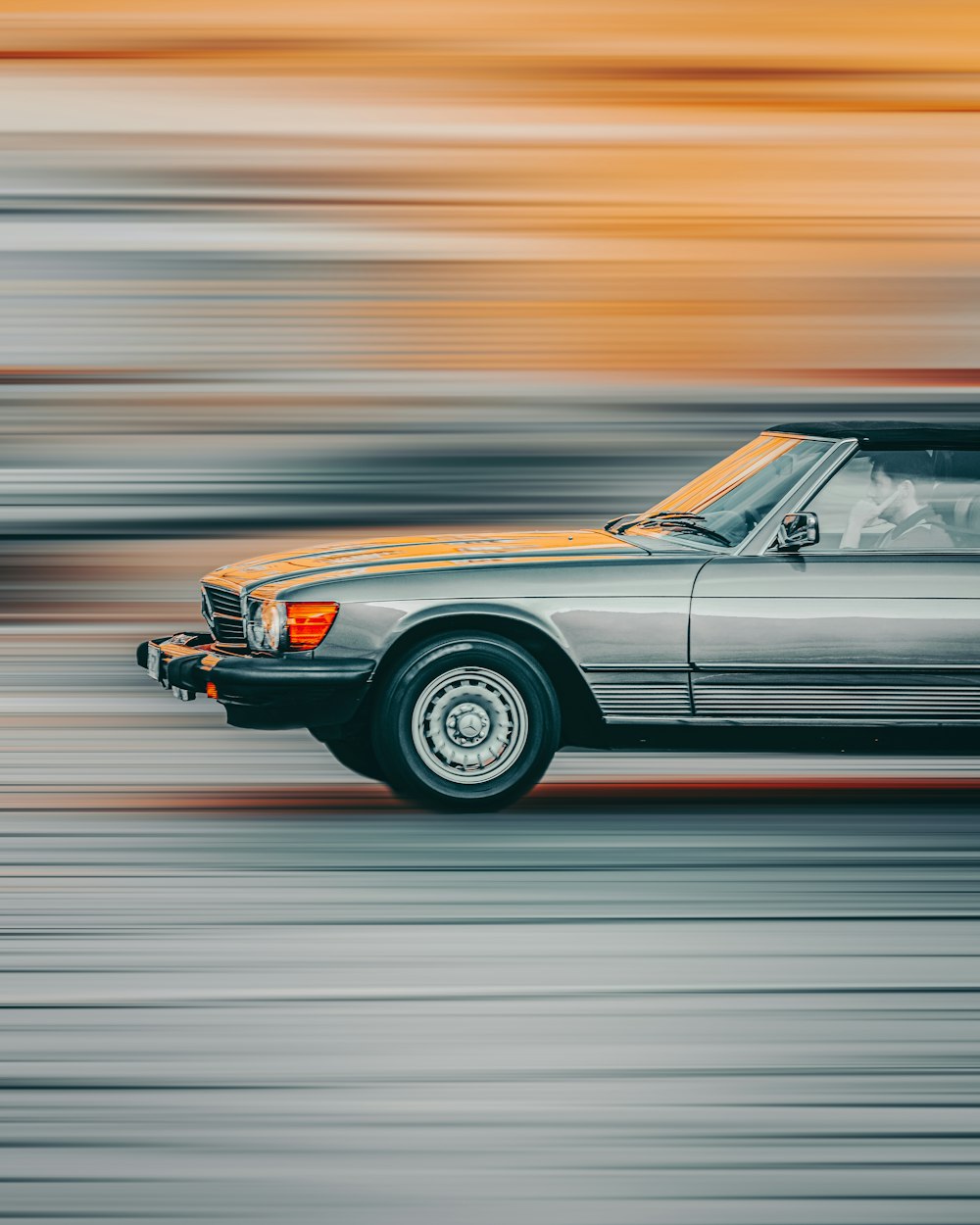 a silver car driving down a street next to a tall building