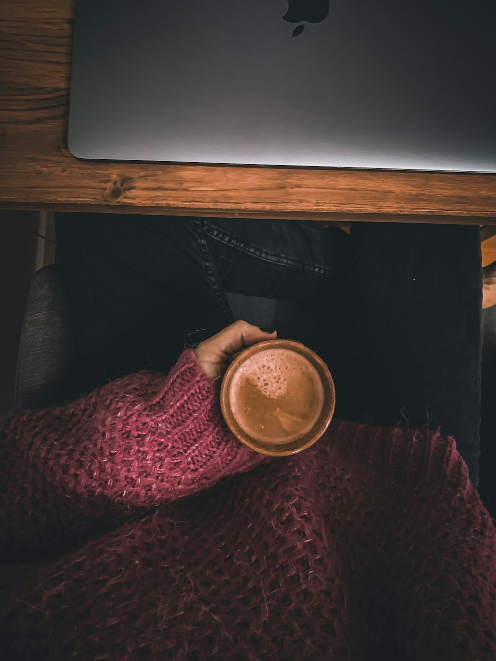 a person holding a cup of coffee under a laptop