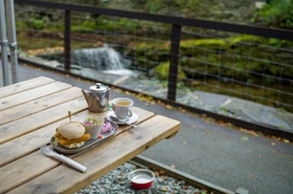 A cozy wooden table with a steaming cup of herbal tea and a small plate of assorted finger sandwiches.
