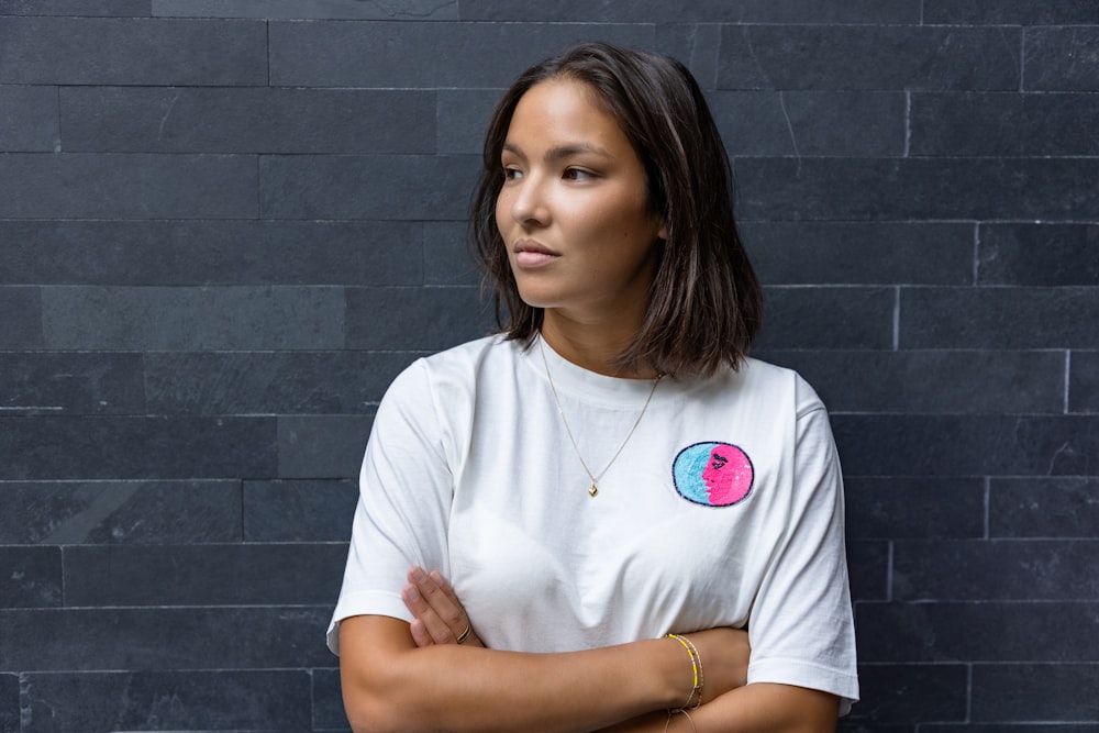 uma mulher de pé com os braços cruzados na frente de uma parede de tijolos