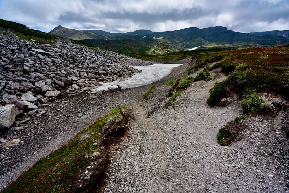 a dirt path with rocks and grass on the side of a mountain