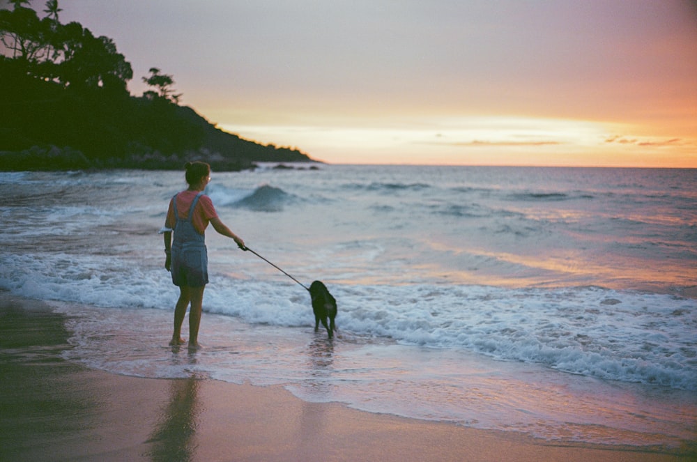 a woman walking her dog on the beach at sunset