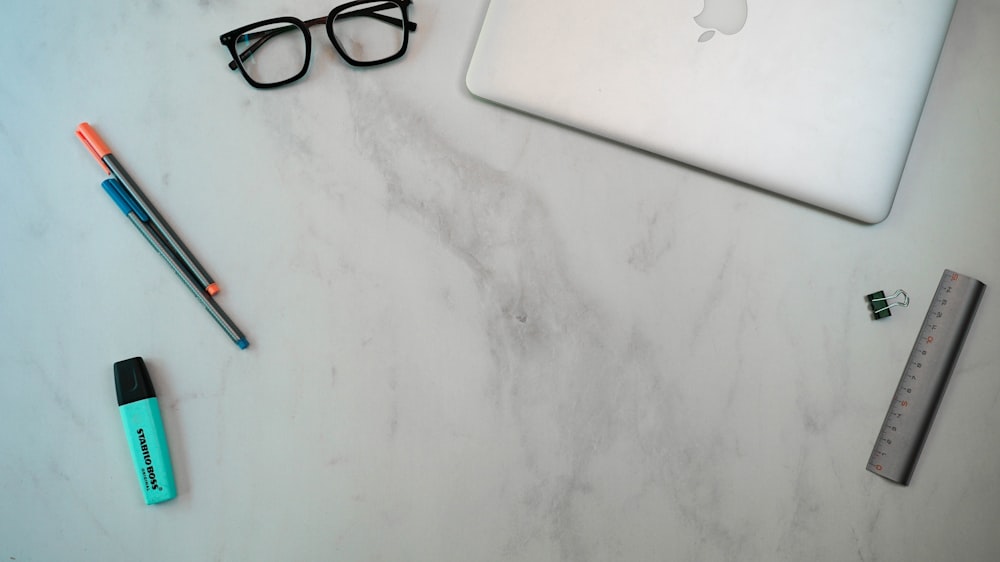 a laptop, pen, ruler, eyeglasses, and pencil on a marble