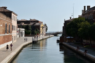 two people walking down a street next to a body of water
