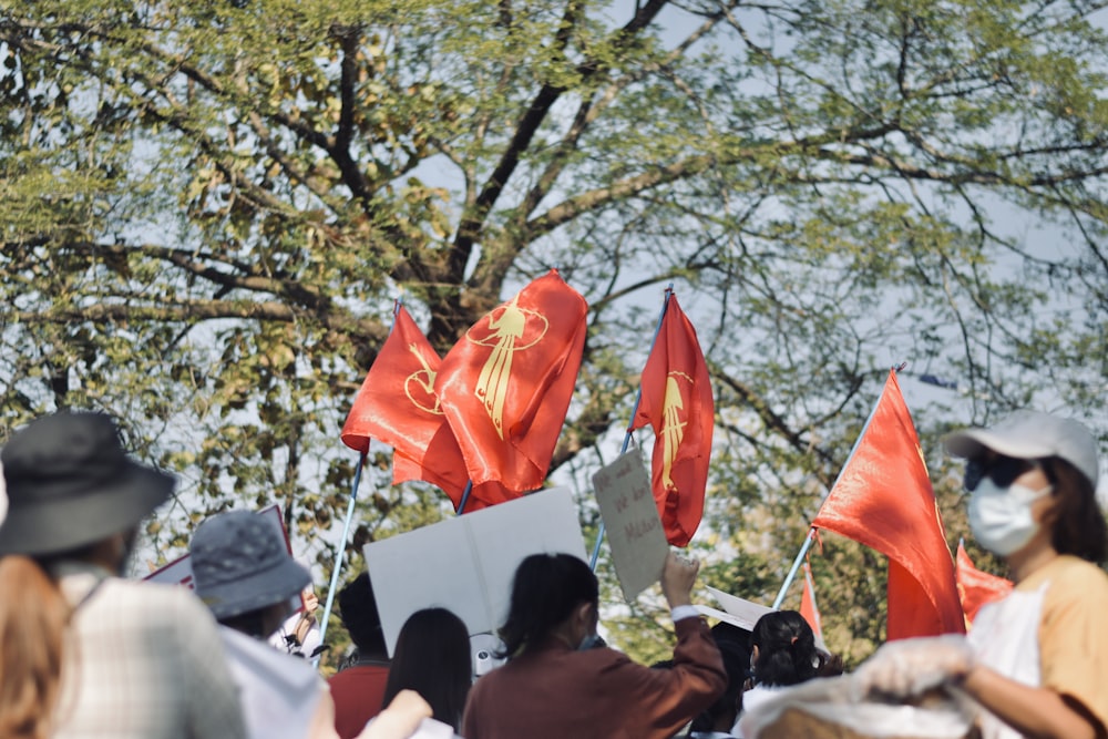 Un grupo de personas con banderas rojas frente a un árbol