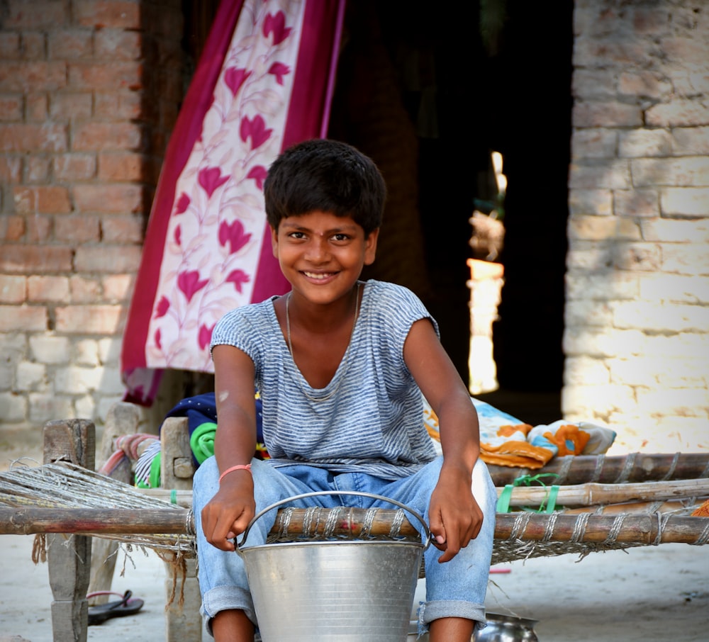 a young boy sitting on a bench holding a bucket