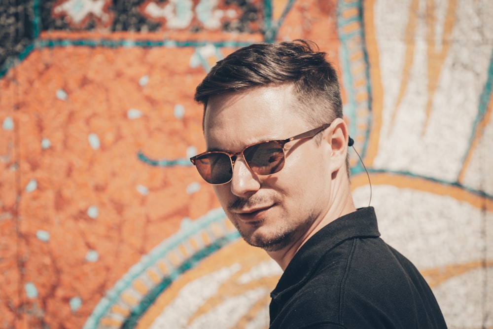 a man wearing sunglasses standing in front of a wall