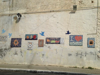 A sunlit wall adorned with a large mosaic depicting traditional Mani landscapes.