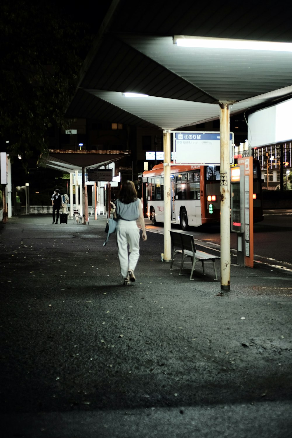 a woman walking towards a bus stop at night