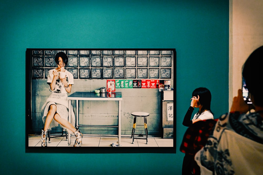 a woman standing in front of a picture of a woman sitting at a table