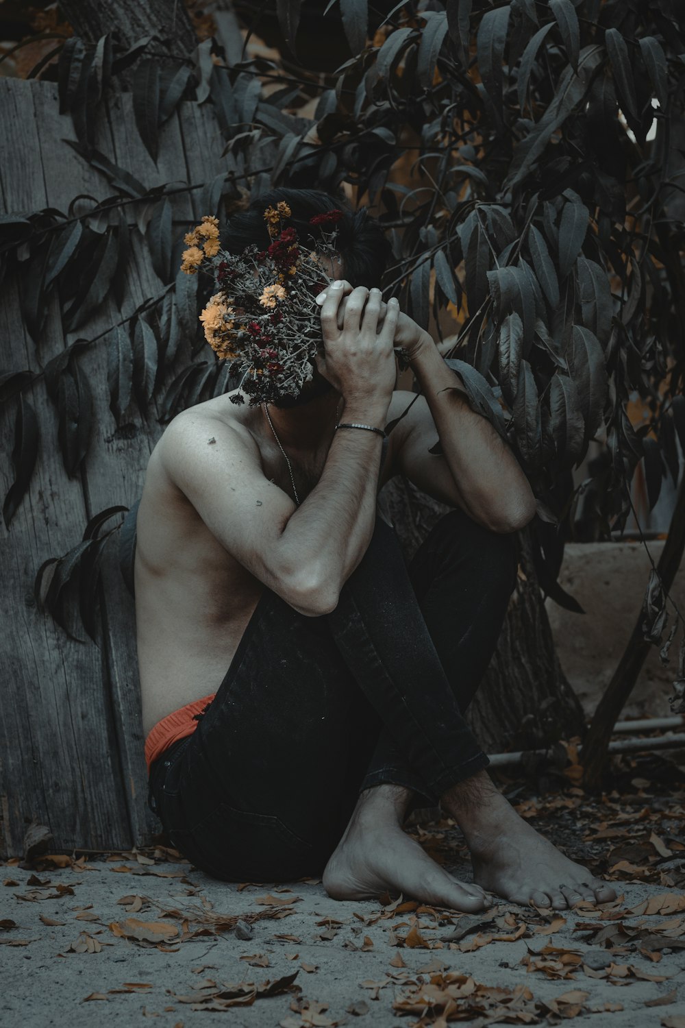 a shirtless man sitting on the ground next to a tree