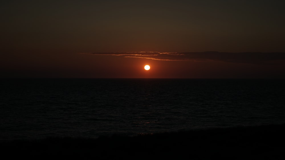 the sun is setting over the ocean on a cloudy day