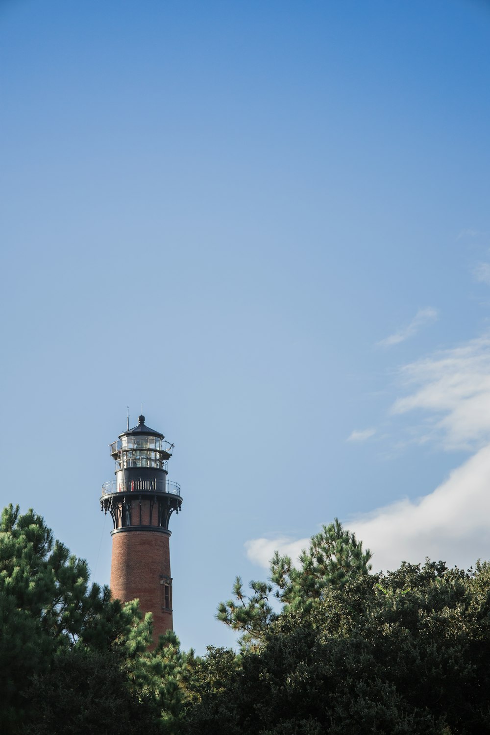 a tall light house surrounded by trees under a blue sky