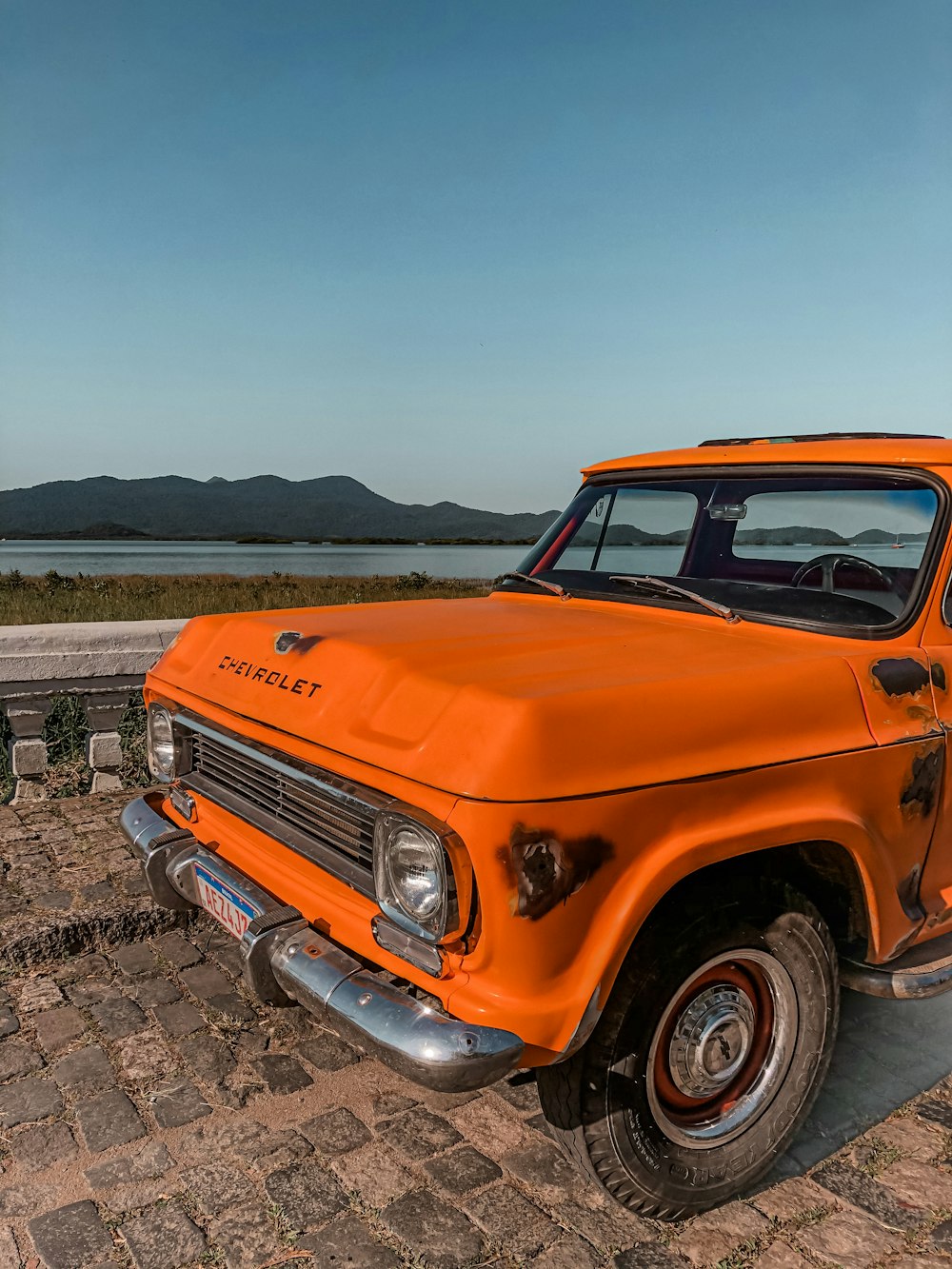 an orange pick up truck parked on a cobblestone road