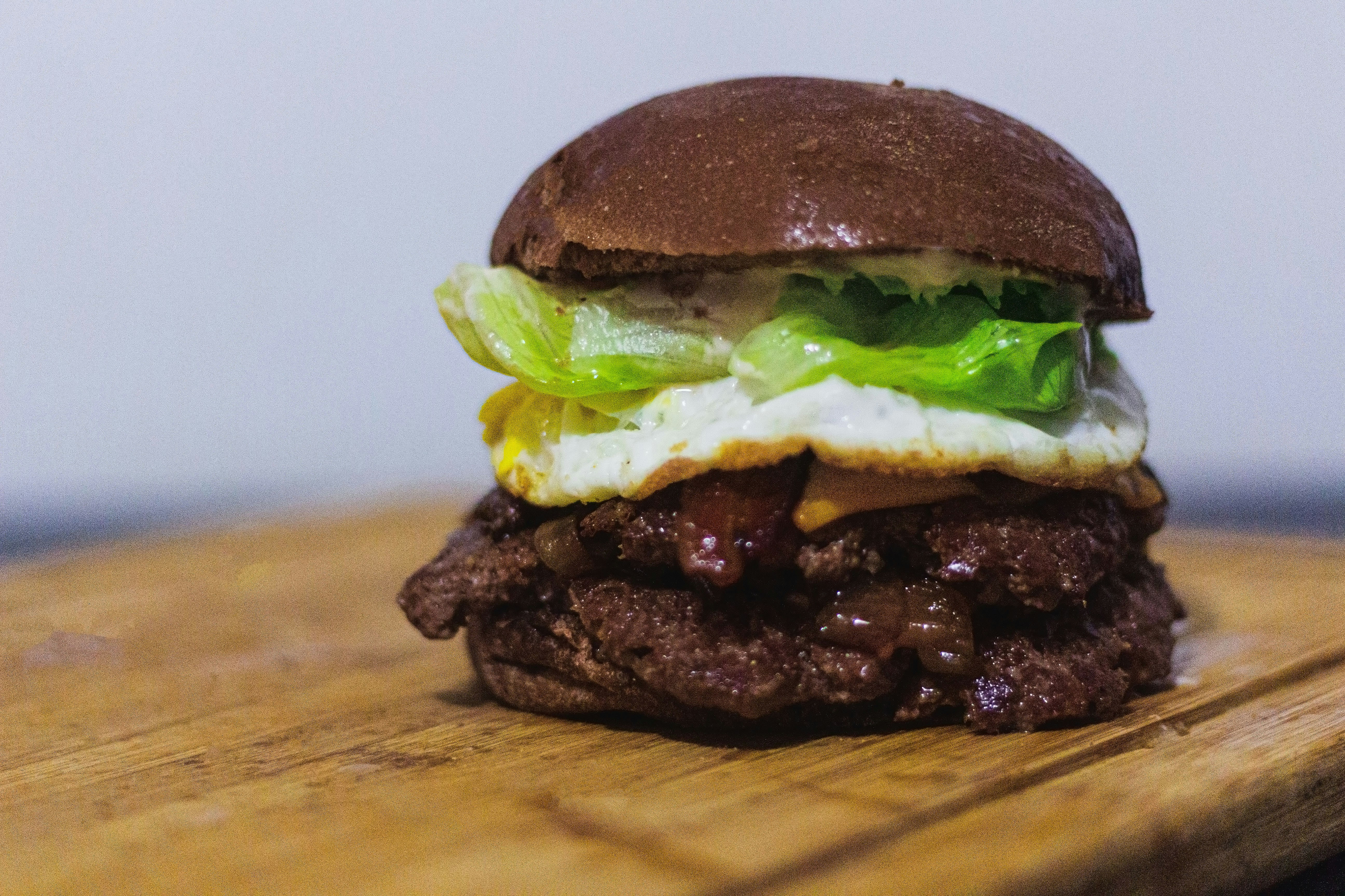 Juicy double patty AKC special burger with lettuce, tomato and golden bun on dark wooden board