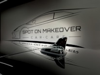 A sleek and glossy surface reflecting a stylized design of a car with the words 'Spot On Makeover Car Care' in a minimalistic and modern font. The image includes a focus on a small shark-fin antenna, emphasizing a clean and sophisticated automotive theme.