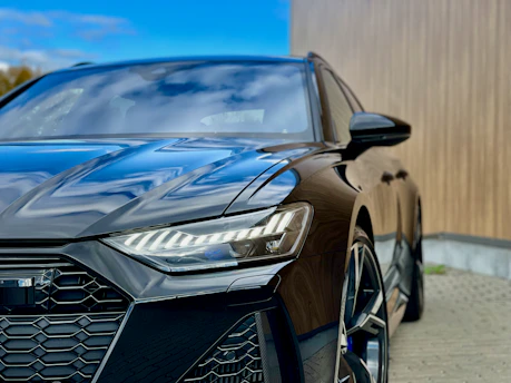 A sleek black car parked in front of carro.com's modern dealership in Cabo Frio under a clear blue sky.