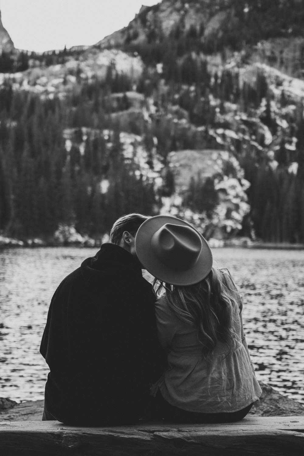 a man and a woman sitting on a dock next to a lake