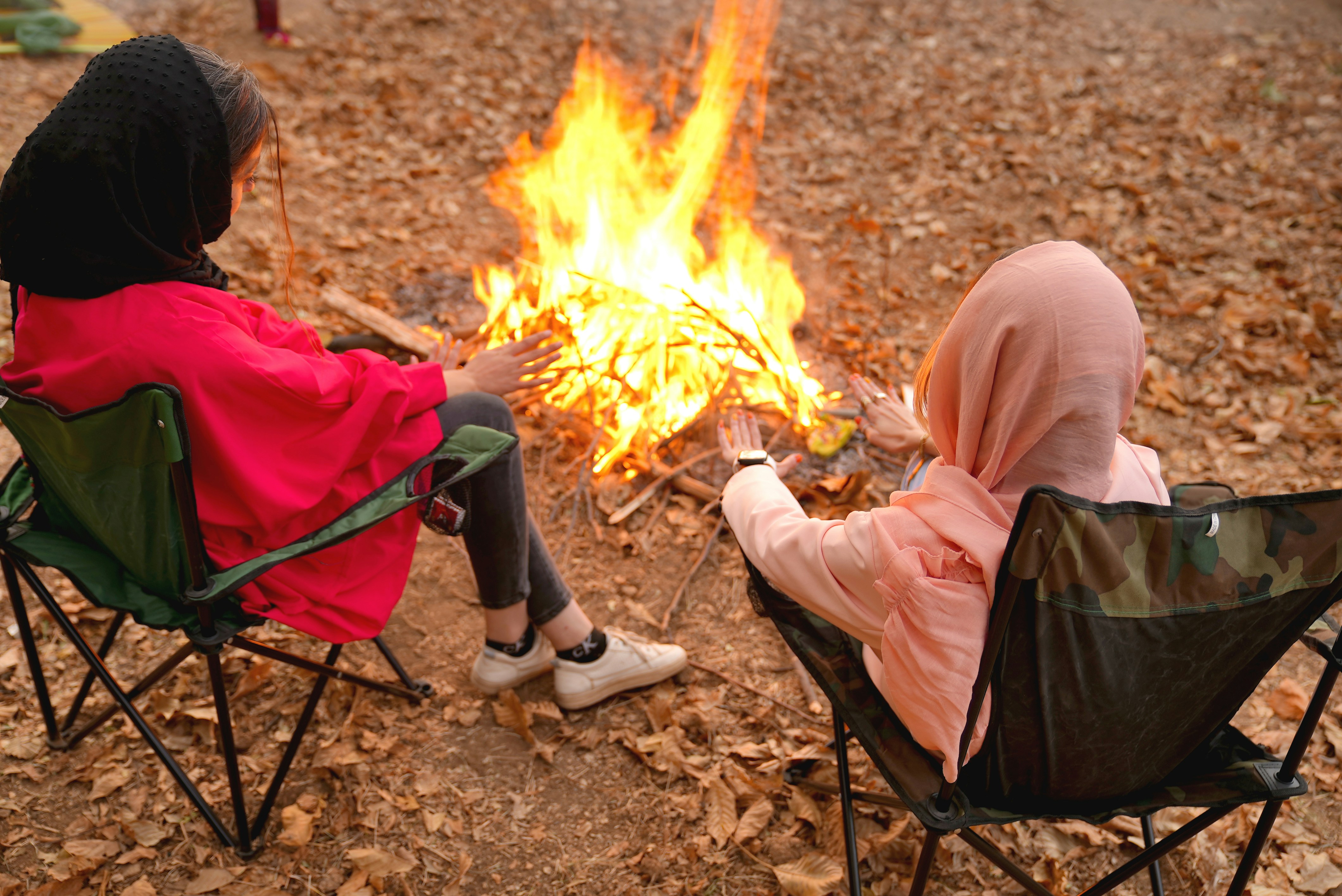 Sitting 2 beautiful girls in front of the fire in autumn nature 