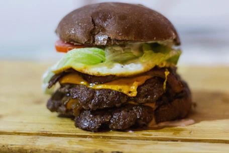 Close-up of a sizzling, stacked burger with melted cheese and fresh toppings on a dark rustic plate.