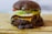 Close-up photo of a perfectly stacked smash burger with melted cheese and fresh toppings on a rustic wooden table.