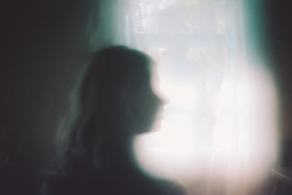 Woman standing before a window in a dimly lit room, solitary contemplation