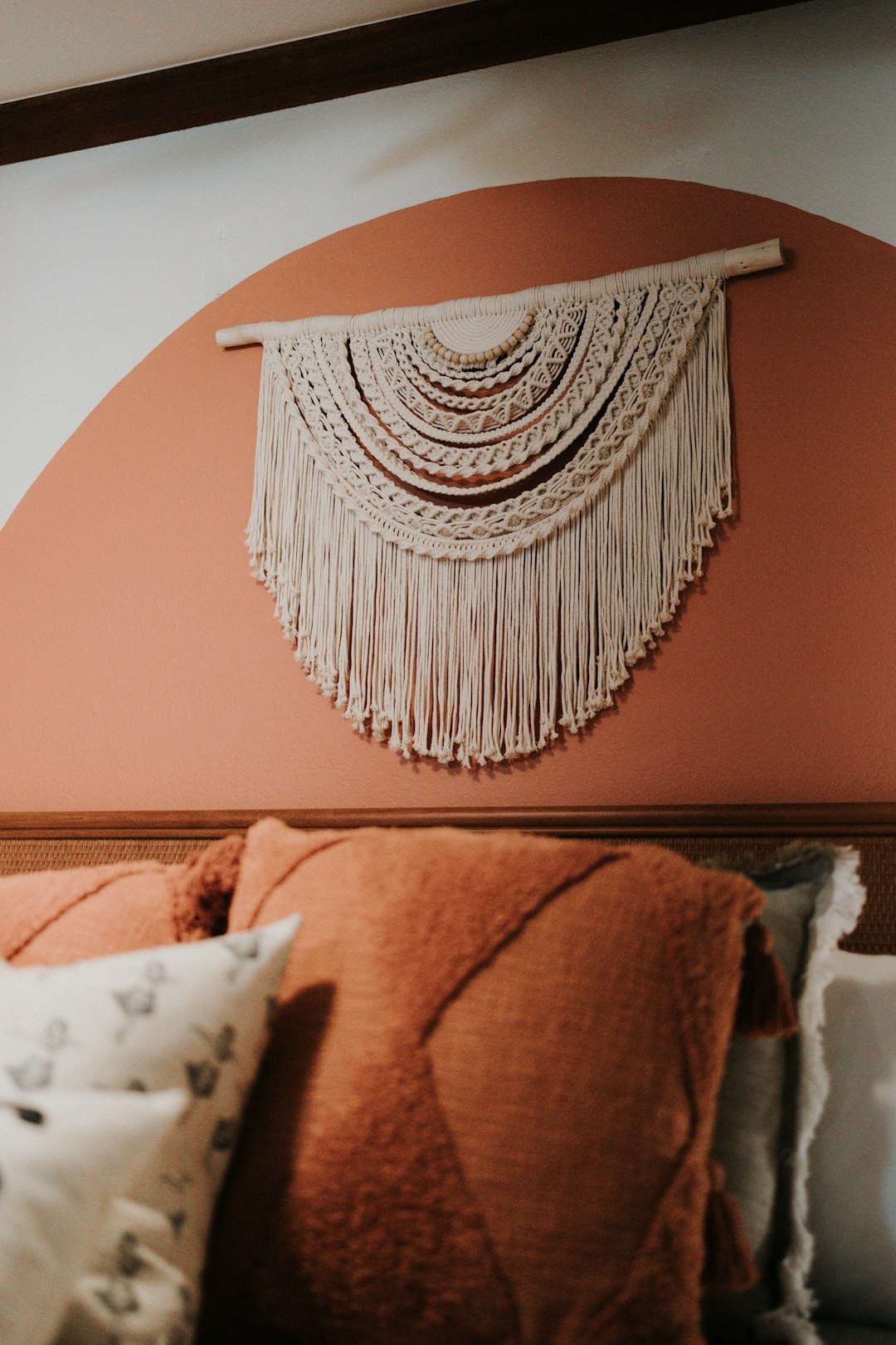 Terracotta painted arch on the wall behind a macrame hanging and pillows
