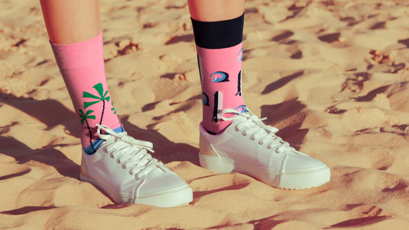 Bright pink palm-print socks worn with sneakers on golden sand