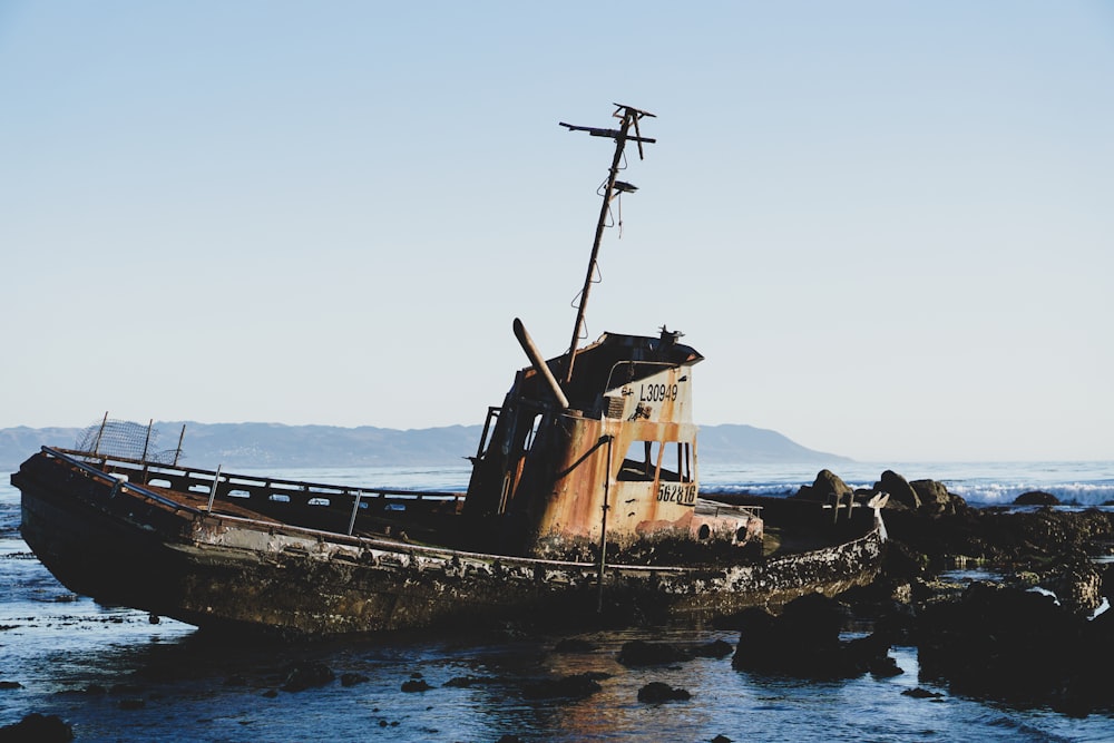a rusted boat sitting on top of a rocky beach