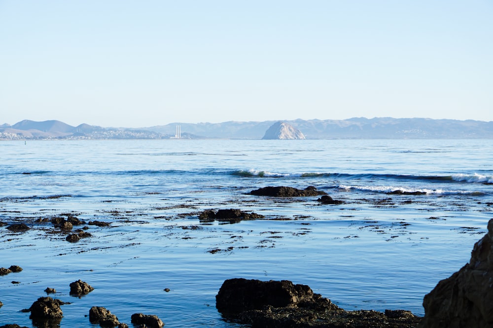 a body of water with rocks in the foreground and mountains in the background