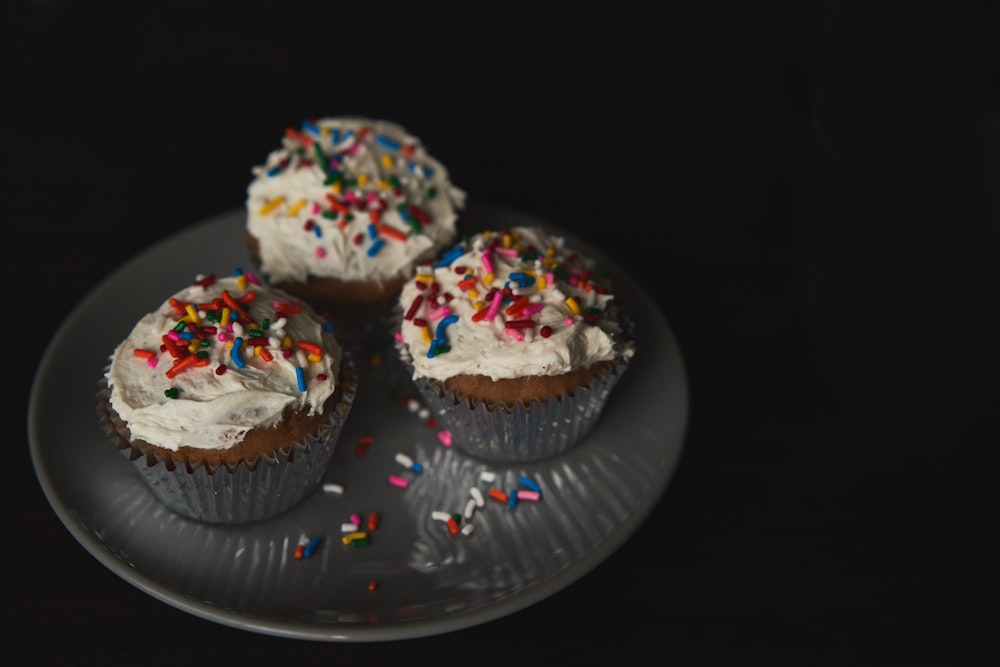 three cupcakes with white frosting and sprinkles on a plate