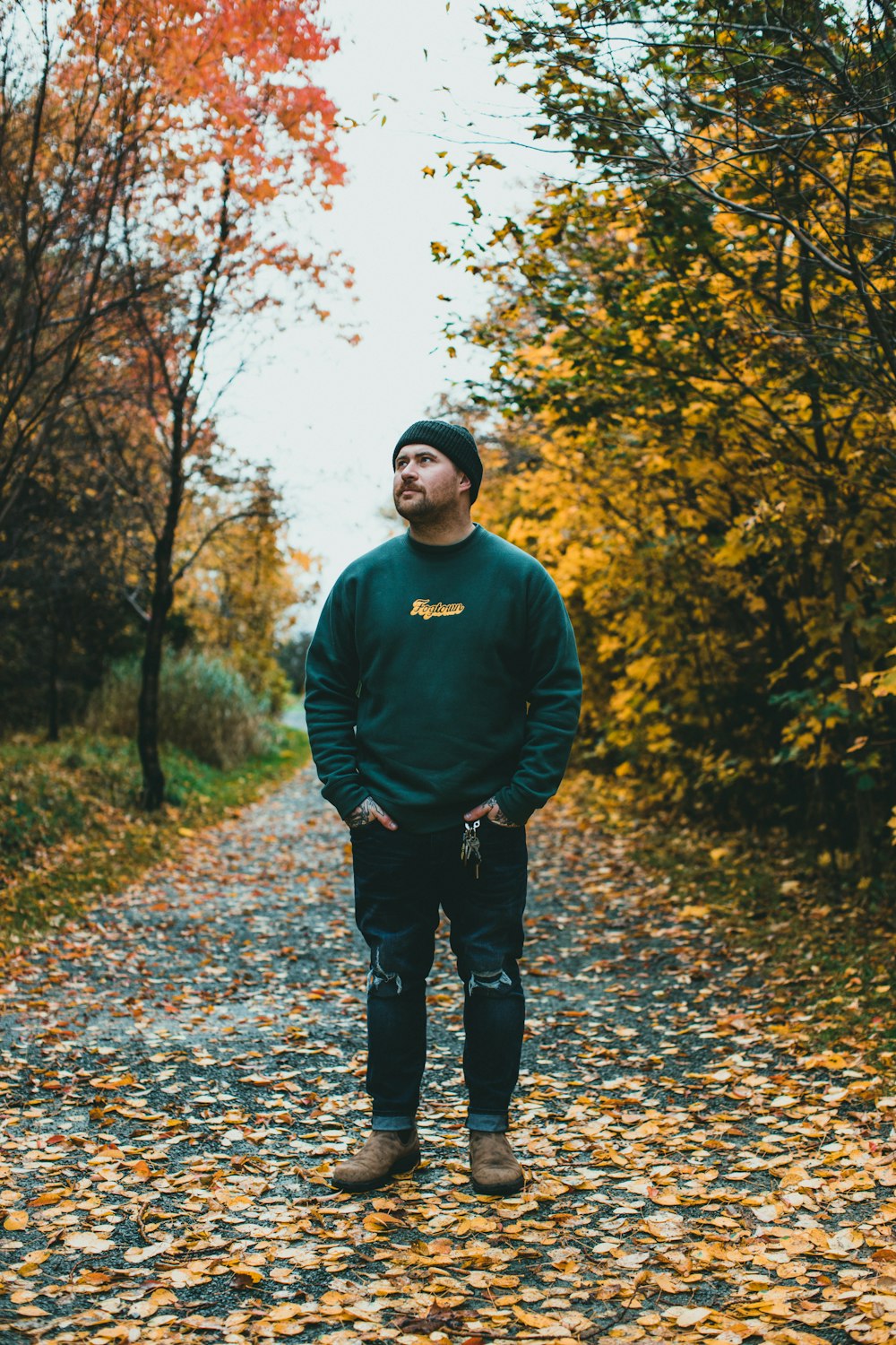 a man standing in the middle of a leaf covered road