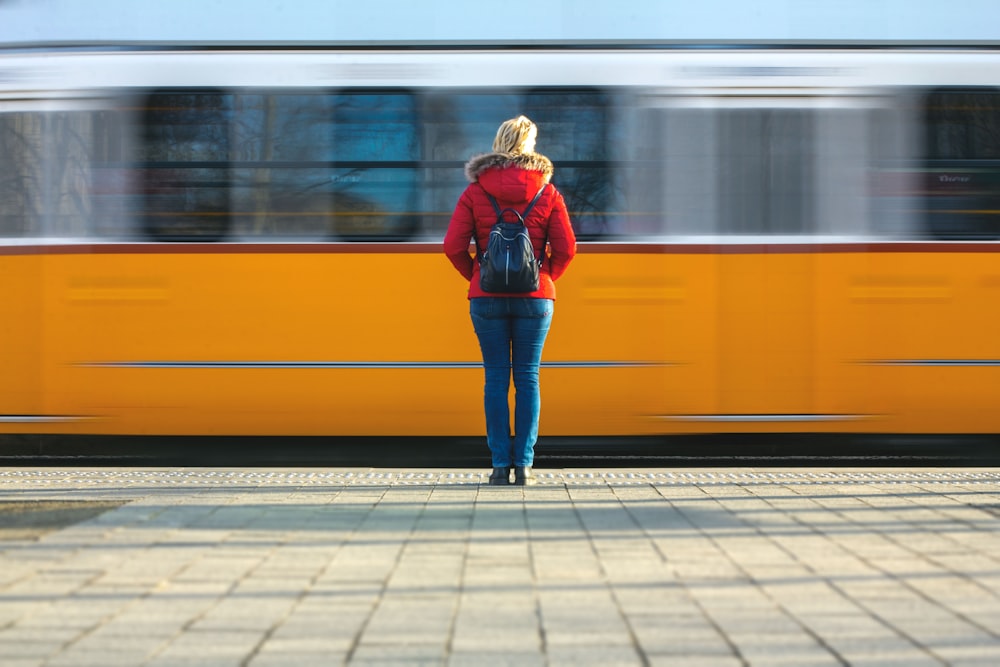 a woman in a red jacket is waiting for a train