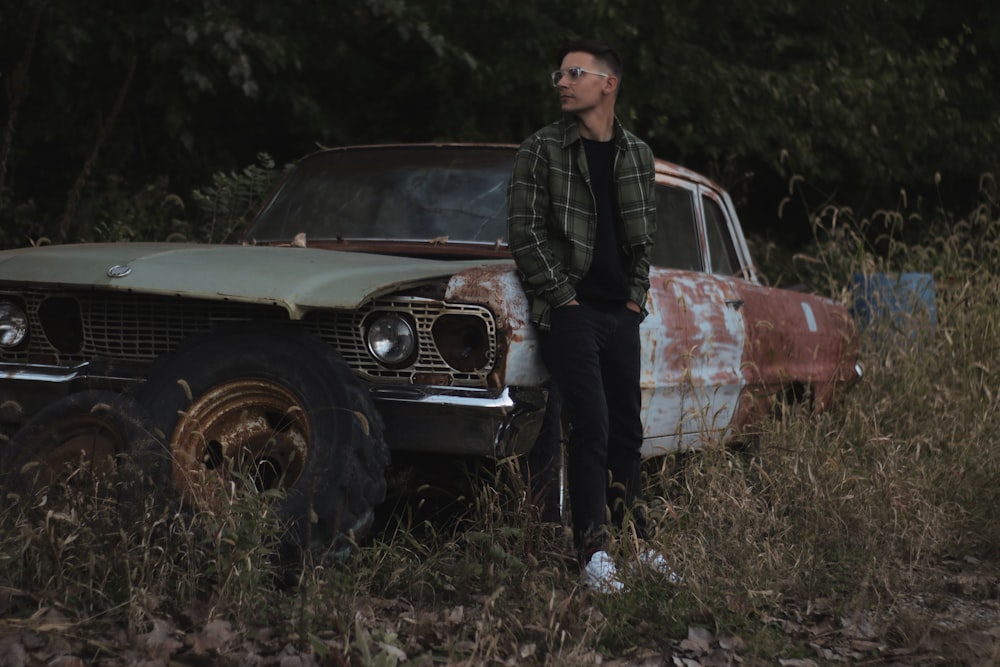 a man standing next to an old car in a field
