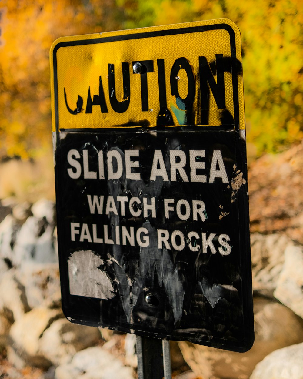 a black and yellow sign that says caution slide area watch for falling rocks