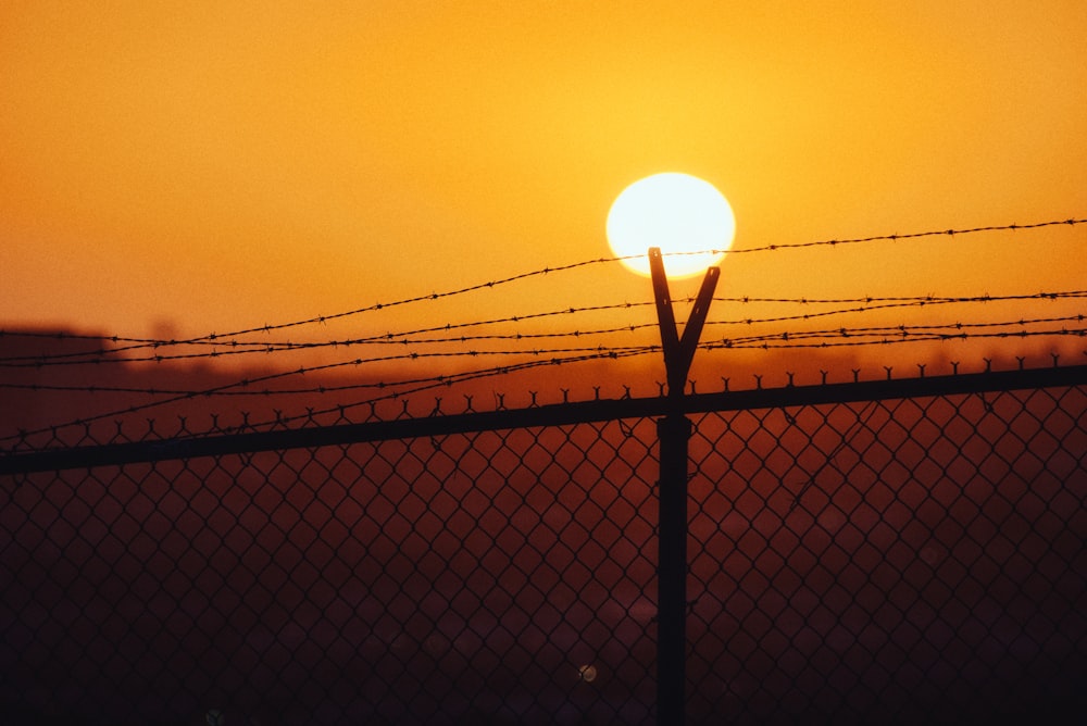 the sun is setting behind a barbed wire fence