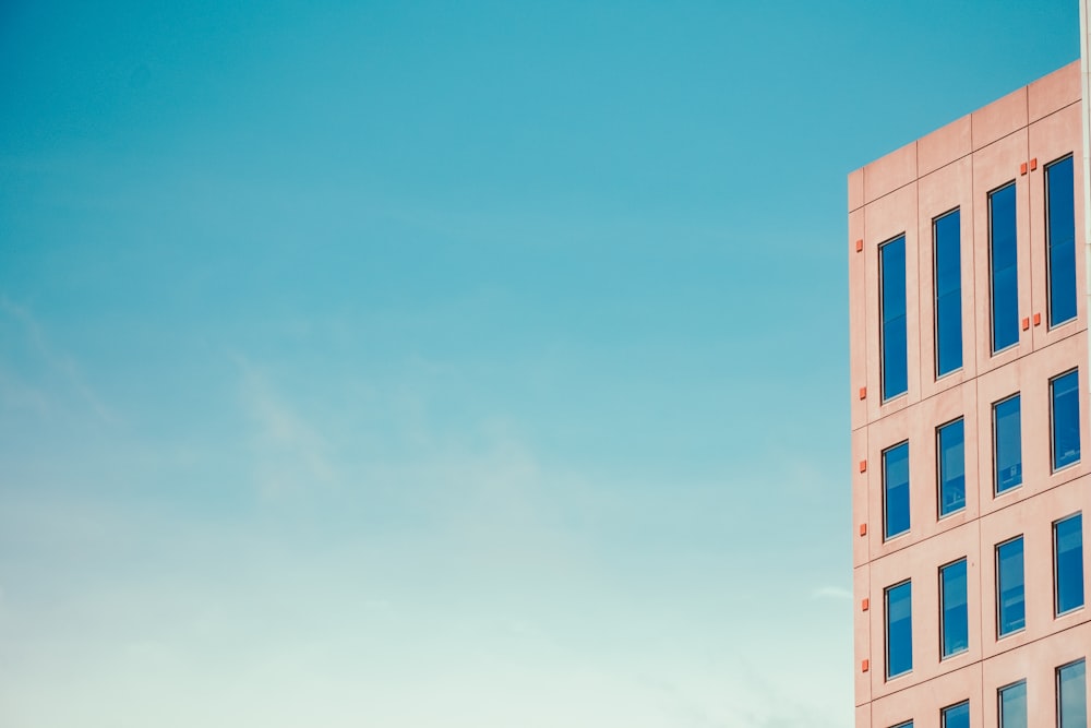 a tall pink building with blue windows against a blue sky