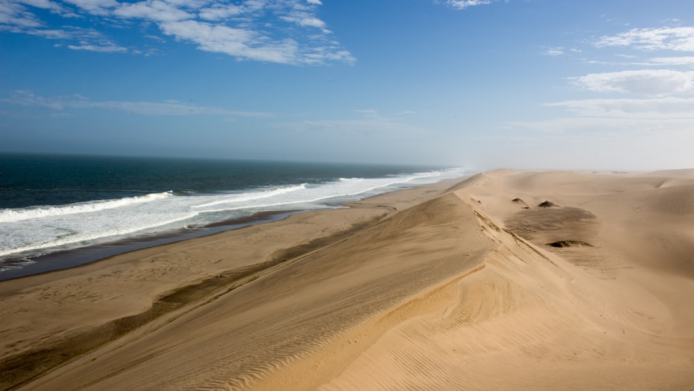 a sandy beach next to the ocean under a blue sky