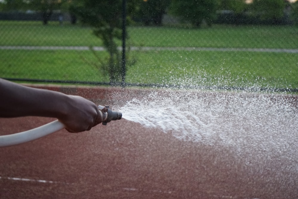 Eine Person sprüht Wasser auf einen Tennisplatz