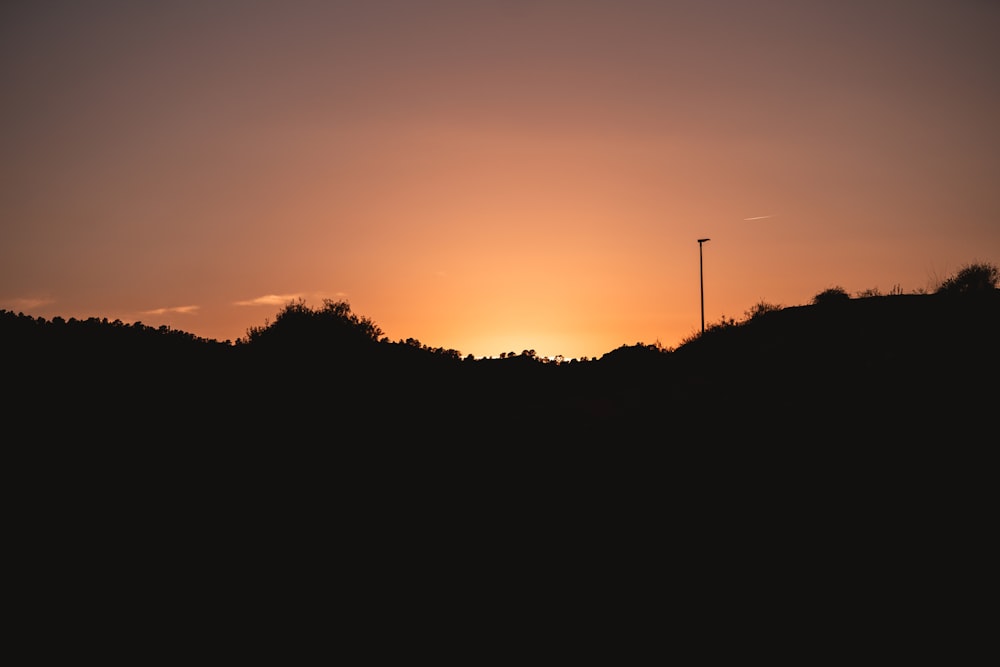 the sun is setting over a hill with trees